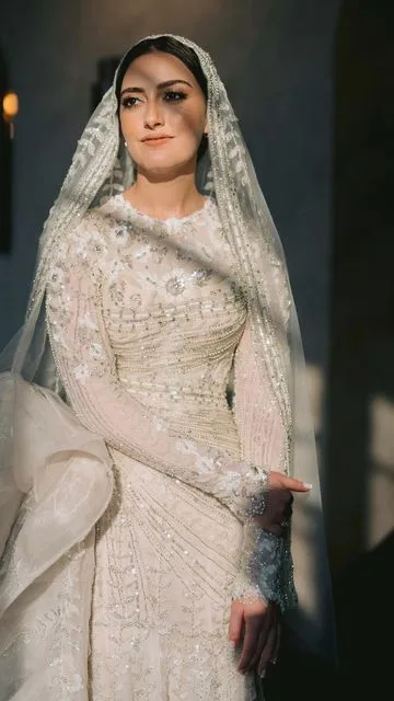 Elegant arabic bridal gown in maroon and gold, with dupatta, in an arched hall.